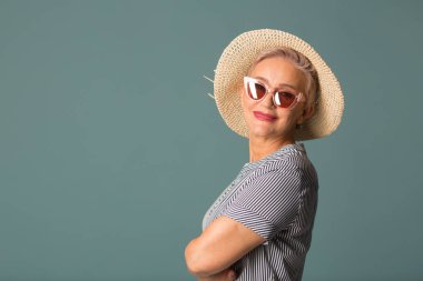 Güneş gözlüklü, mavi arka planda şapkalı yaşlı bir kadın.