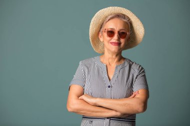 Güneş gözlüklü, mavi arka planda şapkalı yaşlı bir kadın.