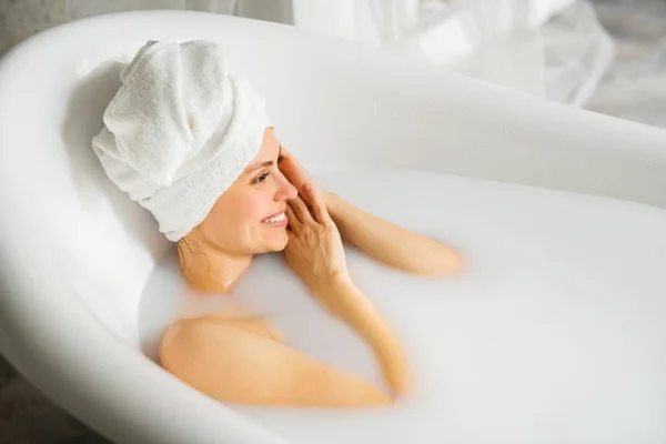 頭にタオルをつけた美しい若い女性がミルクと一緒にお風呂に入ります — ストック写真
