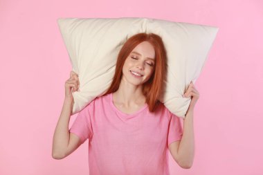 Kızıl saçlı güzel bir kadın pembe arka planda bir yastığın üzerinde yatıyor.