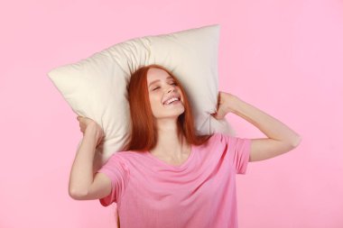 Kızıl saçlı güzel bir kadın pembe arka planda bir yastığın üzerinde yatıyor.