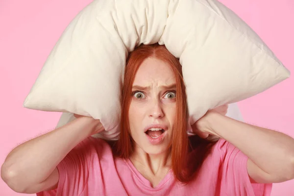 beautiful young woman with red hair with a pillow on her head on a pink background