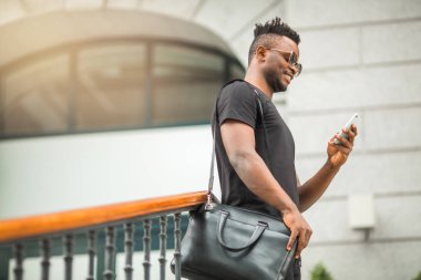 Tişörtlü, elinde telefon olan yakışıklı bir Afrikalı.