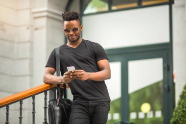 Tişörtlü, elinde telefon olan yakışıklı bir Afrikalı.