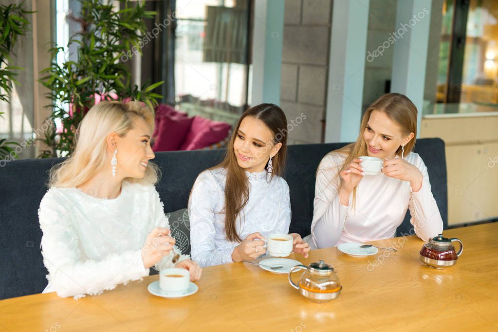 three beautiful young women in white dresses drink tea in a restaurant