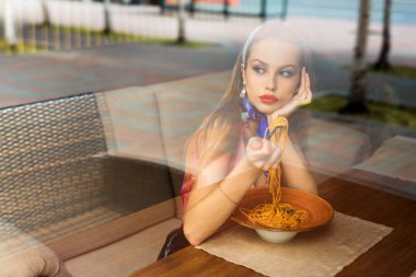 Makyajlı genç bir kadın restoranda spagetti yiyor.