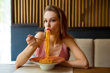 Makyajlı genç bir kadın restoranda spagetti yiyor.