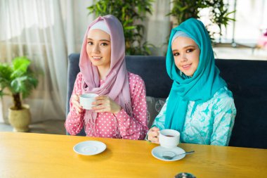İki güzel genç kadın, bir restoranda, Müslüman elbiseleriyle çay içiyorlar.