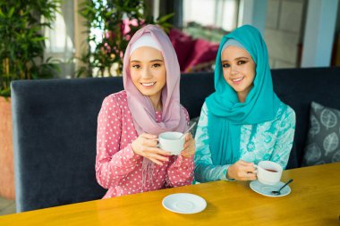 İki güzel genç kadın, bir restoranda, Müslüman elbiseleriyle çay içiyorlar.