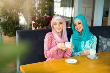 İki güzel genç kadın, bir restoranda, Müslüman elbiseleriyle çay içiyorlar.