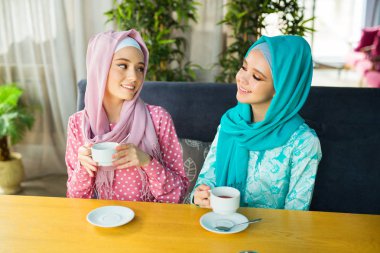 İki güzel genç kadın, bir restoranda, Müslüman elbiseleriyle çay içiyorlar.