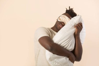 Elinde yastıkla bej arka planda yakışıklı bir Afrikalı.