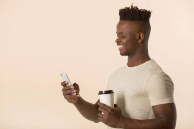 Elinde bir bardak kahveyle bej arka planda yakışıklı bir Afrikalı.