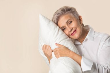 Bej bir arka planda yastığı olan şık, güzel, yaşlı bir kadın.