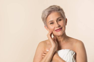 Beyaz havluyla bej arka planda şık, güzel, yaşlı bir kadın.