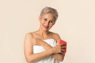 Beyaz havluyla bej arka planda güzel, yaşlı bir kadın yıkanır.