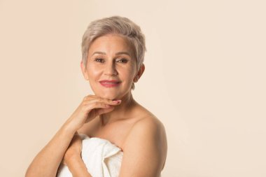 Beyaz havluyla bej arka planda şık, güzel, yaşlı bir kadın.