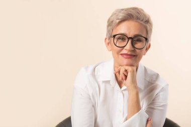 Kısa saçlı, bej arka planda beyaz gömlekli şık, güzel bir kadın.