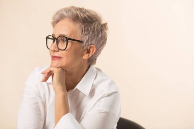 Kısa saçlı, bej arka planda beyaz gömlekli şık, güzel bir kadın.