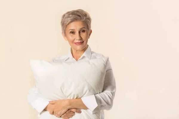 Bej bir arka planda yastığı olan şık, güzel, yaşlı bir kadın.