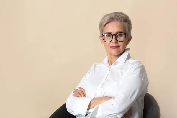 Kısa saçlı, bej arka planda beyaz gömlekli şık, güzel bir kadın.