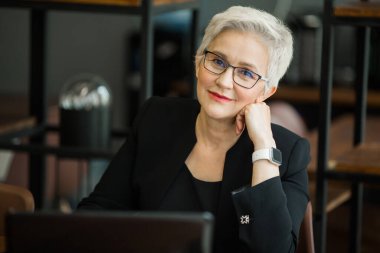 Siyah takım elbiseli güzel, şık bir kadın iş yerinde dizüstü bilgisayarla oturuyor.