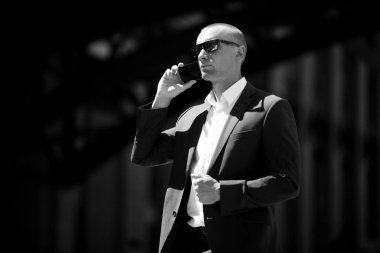 takım elbiseli ve gözlüklü telefonlu bir adamın siyah beyaz portresi.