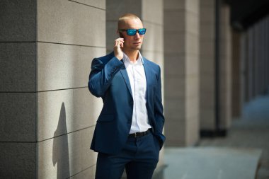 Yazlık takım elbiseli, güneş gözlüklü, elinde telefon olan yakışıklı bir genç.