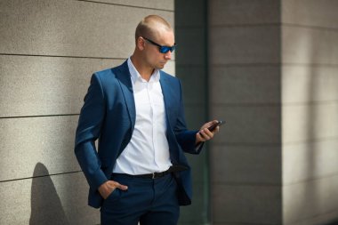 Yazlık takım elbiseli, güneş gözlüklü, elinde telefon olan yakışıklı bir genç.