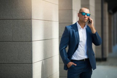 Yazlık takım elbiseli, güneş gözlüklü, elinde telefon olan yakışıklı bir genç.