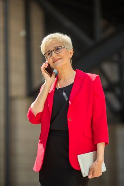 Kısa saçlı, kırmızı ceketli ve telefonlu güzel, yaşlı bir kadın.