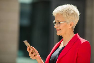 Kısa saçlı, kırmızı ceketli ve telefonlu güzel, yaşlı bir kadın.