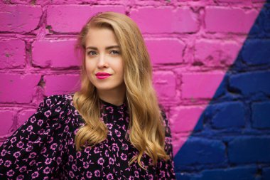 Güzel genç bir kadın, parlak renkli bir duvarın yanında.