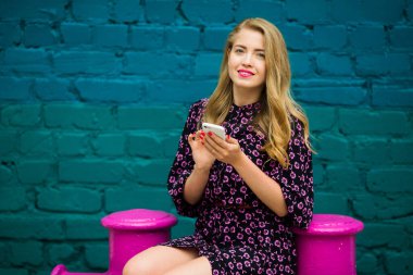 Parlak renkli bir duvarın yanında telefonu olan güzel genç bir kadın.