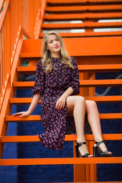 一个穿着裙子的年轻貌美的女人靠近一个明亮的橙色楼梯 — 图库照片