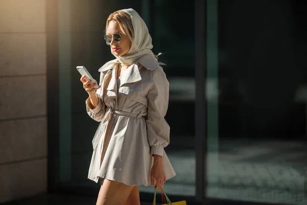 코트와 선글라스를 전화기와 소포를 아름다운 아가씨 — 스톡 사진