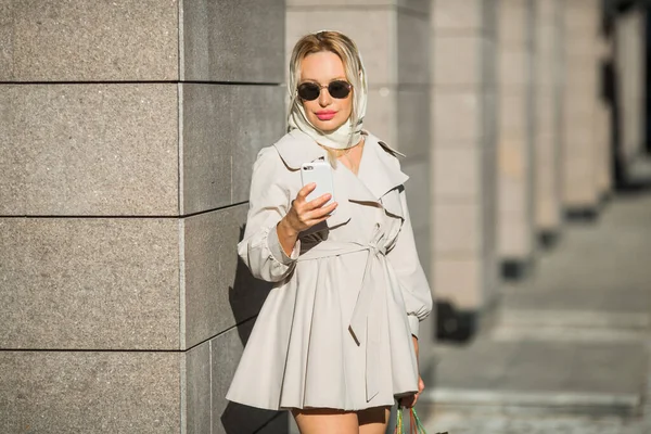 코트와 선글라스를 전화기와 소포를 아름다운 아가씨 — 스톡 사진