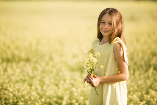 黄色のドレスを着た10代の少女が夏に黄色い畑で花を摘む — ストック写真