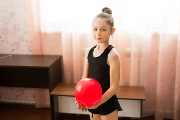 beautiful young teenage girl in sportswear is engaged in gymnastics at home with a ball