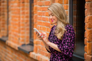 Yazlık bir elbise içinde, duvar arkasında cep telefonuyla güzel bir bayan.