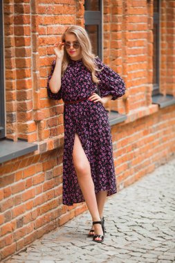 Tuğla duvarda güneş gözlüğü takmış, yaz elbisesi giymiş güzel genç bir kadın.