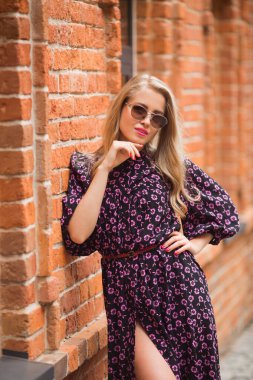 Tuğla duvarda güneş gözlüğü takmış, yaz elbisesi giymiş güzel genç bir kadın.