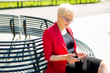 Kısa saçlı ve elinde tabletle gözlüklü yaşlı güzel bir kadın.
