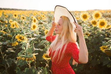 Ayçiçekli bir tarlada şapkası olan kırmızı elbiseli güzel bir kadın.