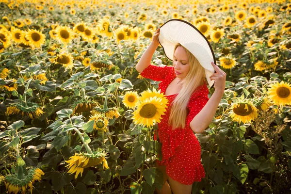 ひまわり畑に帽子をかぶった赤いドレスを着た美しい若い女性 — ストック写真