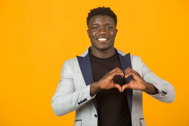 Ceketli, sarı arka planda, el hareketleriyle yakışıklı, genç Afrikalı bir erkek.