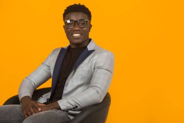 Sarı arka planda ceketli, gözlüklü yakışıklı Afrikalı bir erkek.