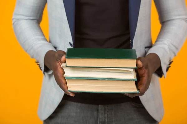 african male in jacket, with books on yellow background