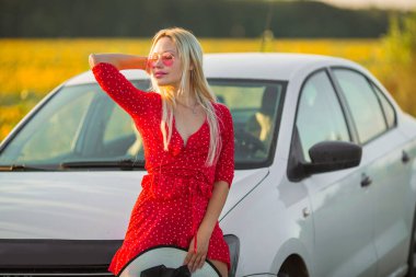 Yazın arabanın yanında pembe gözlüklü, kırmızı elbiseli güzel bir kadın.