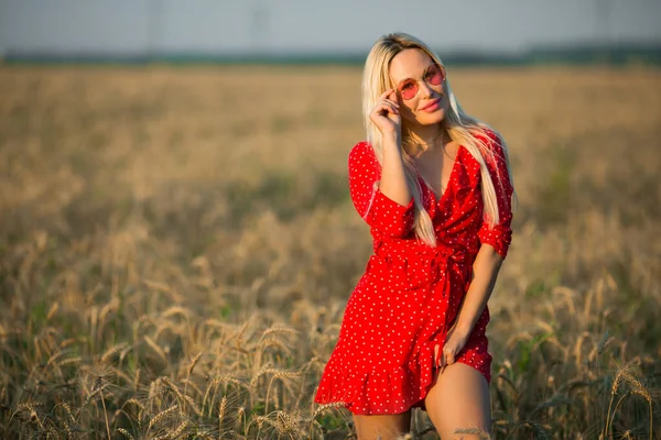 ピンクのサングラスの夏の畑に赤いドレスを着た美しい若い女性 — ストック写真